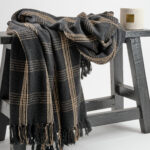 Plaid tissé à carreaux noir et beige avec franges fabriqué à partir de vêtements recyclés. Utilisable sur un canapé ou en jeté de lit.