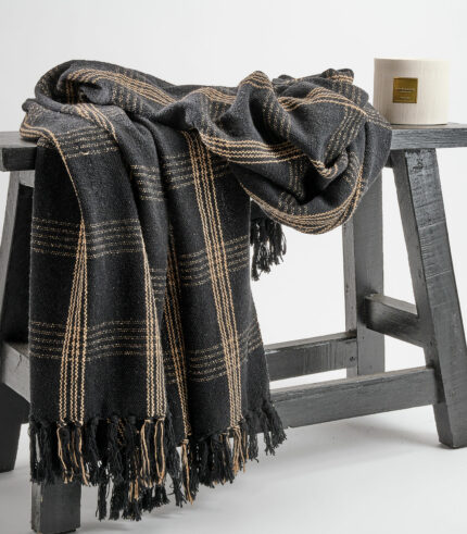 Plaid tissé à carreaux noir et beige avec franges fabriqué à partir de vêtements recyclés. Utilisable sur un canapé ou en jeté de lit.